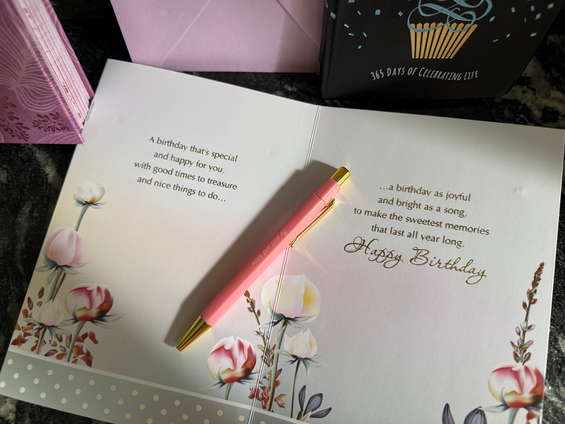Open birthday card with floral design, pen, and pink envelope on a textured surface