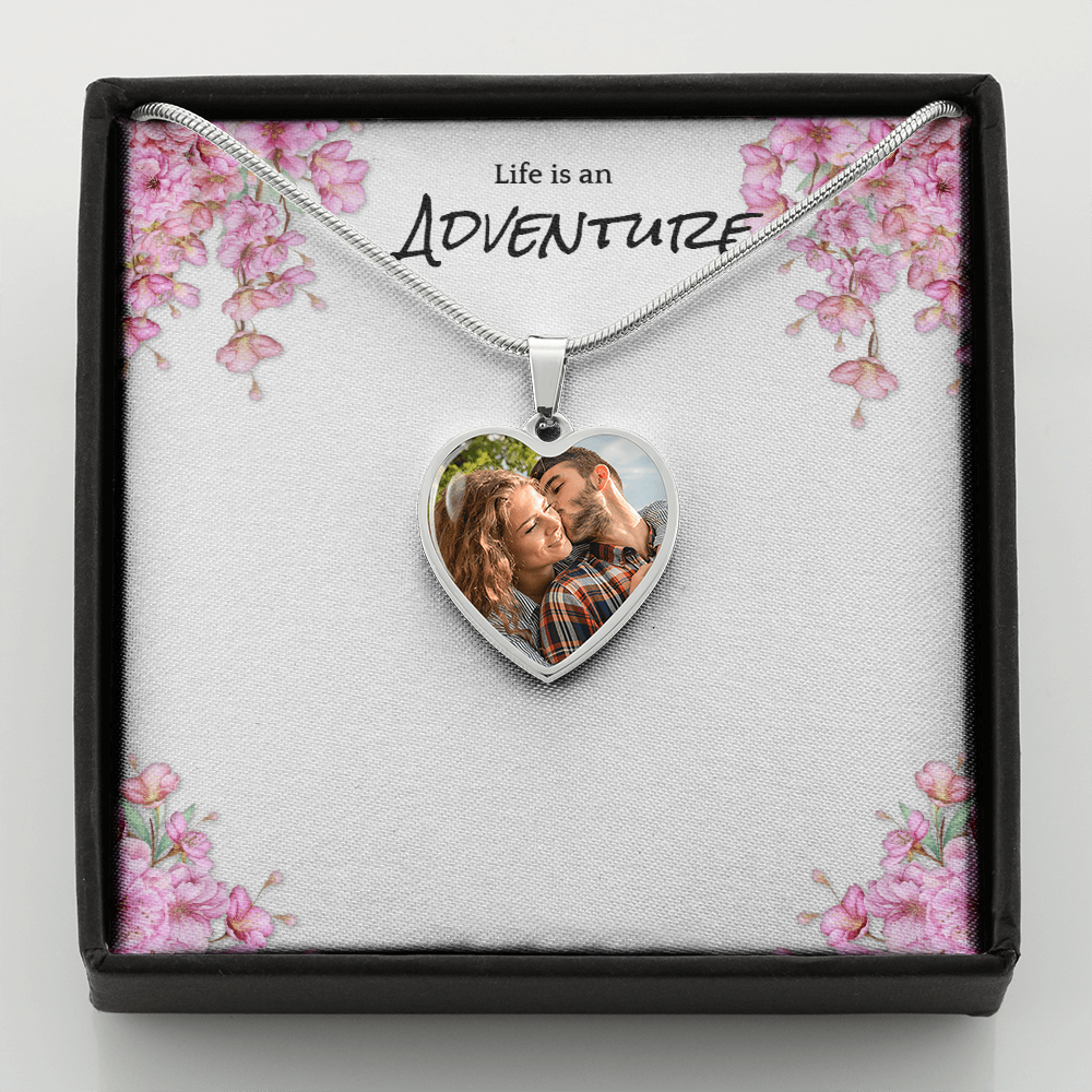 Heart-shaped necklace with a photo of a couple in a decorative box with floral design and 'Life is an Adventure' text.